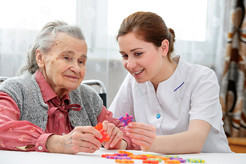 Senior woman wearing grey sweater and a young female nurse helping her with a puzzle
