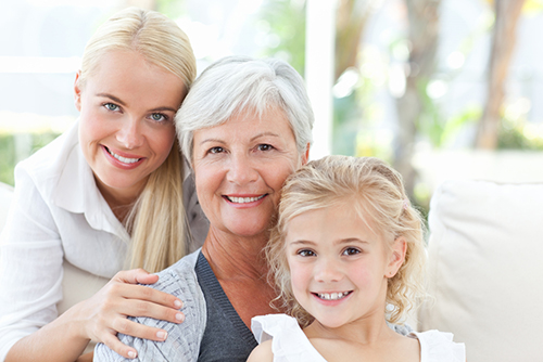 Elderly woman sitting between her blonde daughter and blonde granddaughter smiling